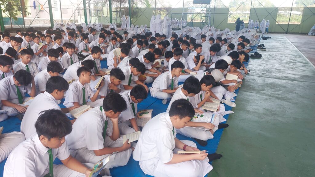 Barisan murid laki-laki SMP Islam Al Azhar 16 Cikarang yang rapi menggunakan seragam putih abu-abu Al Azhar dan peci hitam, berbaris khusyuk saat mengikuti upacara bendera di lapangan sekolah yang asri.